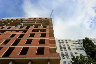 Mavi gökyüzünün arka planında yapım aşamasındaki çok katlı bir bina ve vinç.