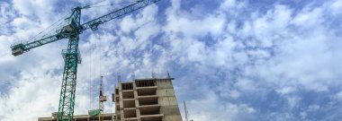 Mavi gökyüzünün arka planında inşaat halindeki çok katlı bir bina ve vinç manzarası