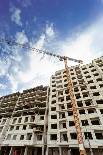 Multi-storey residential building under construction and crane on a background of blue sky