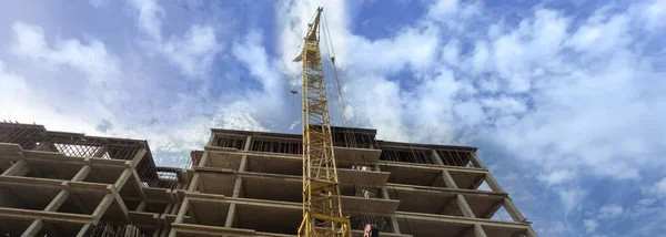 Panorama of a multi-storey residential building under construction and crane on a background of blue sky