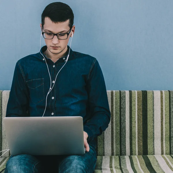 Dizüstü bilgisayar ile kanepede oturan gözlüklü genç adam