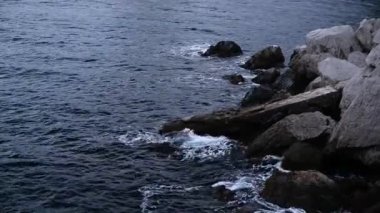 Dalgalar kayaların üzerinden yüksekten görünüyor. Büyük kar beyazı dalgalar.