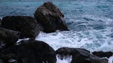 Dalgalar kayaların üzerinden yüksekten görünüyor. Büyük kar beyazı dalgalar.