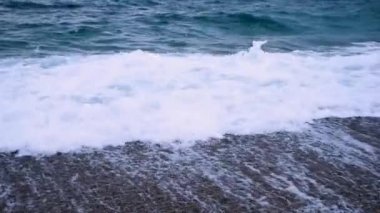 Kumsalda turkuaz dalgalar ve çakıl taşları. Sahildeki dalgalardan köpük.