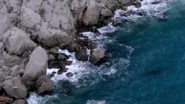 Dalgalar kayaların üzerinden yüksekten görünüyor. Büyük kar beyazı dalgalar.