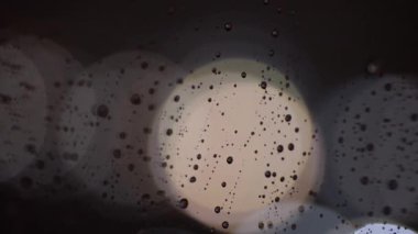 Geceleri bardaktan yağmur damlaları akıyor. Bokeh 'in arka planındaki cama yağmur damlaları damlıyor. Geceleri pencerenin dışında yağmur yağar