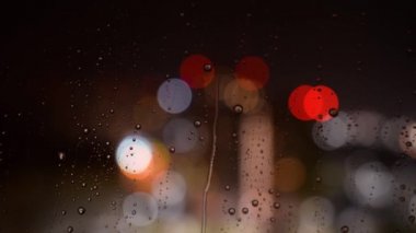 Geceleri bardaktan yağmur damlaları akıyor. Bokeh 'in arka planındaki cama yağmur damlaları damlıyor. Geceleri pencerenin dışına yağmur yağar. Pencerenin dışında gök gürültüsü ve şimşek çakıyor