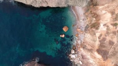 Şeffaf turkuaz deniz kıyısında kayalık bir plajda, kayalar ve kayalar üzerinde dalgaların kırılışının kuş bakışı görüntüsü. Mavi okyanus dalgaları.