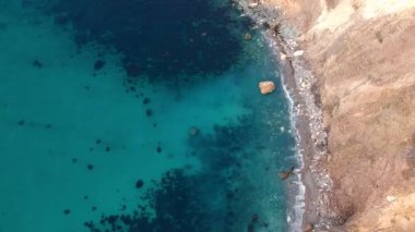 Şeffaf turkuaz deniz kıyısında kayalık bir plajda, kayalar ve kayalar üzerinde dalgaların kırılışının kuş bakışı görüntüsü. Mavi okyanus dalgaları.