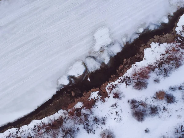 The forest and the frozen river with thawed patches appeared in the spring, when there is still snow in Russia from the height of the quadrocopter