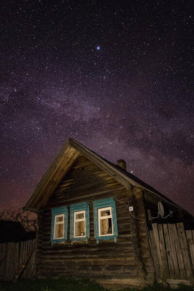 A typical house in a Russian village at night against a starry sky with a milky way