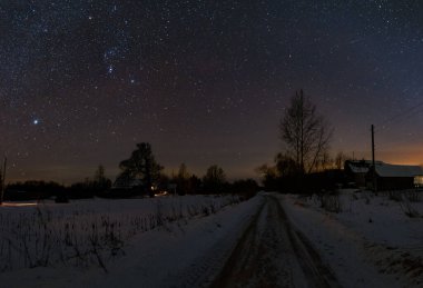 Rus köyündeki yol, geceleri soğuk ve karlı. Ağaçlar ve yukarıdaki yıldızlı gökyüzü. Orion takımyıldızı gökyüzünde parlıyor..
