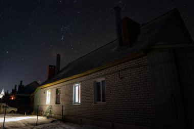 Rus köyündeki ev buz gibi açık bir gecede. Orion 'un takımyıldızı yıldızlı gökyüzünde. Pencerelerde ışıklar yanıyor ve pipo dumanlı..