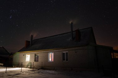 Rus köyündeki ev buz gibi açık bir gecede. Orion 'un takımyıldızı yıldızlı gökyüzünde. Pencerelerde ışıklar yanıyor ve pipo dumanlı..