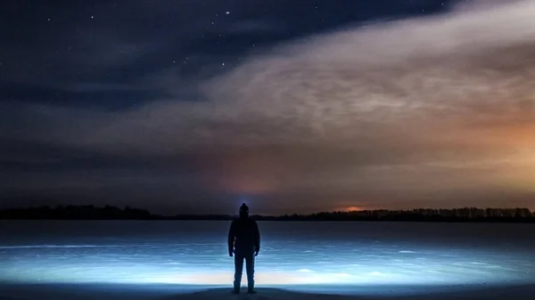 Kafasında fener olan bir adam ayakta duruyor ve bulutlu güzel yıldızlı gökyüzüne bakıyor. Karlı bir arazide. Kış, soğuk bir gece.