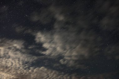 Bir yaz gecesinde ay ışığında bulutların arasından yıldızlar geçiyor.