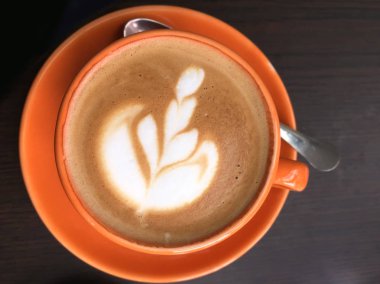 Turuncu bardakta kapuçino ve köpüklü çiçek deseni.