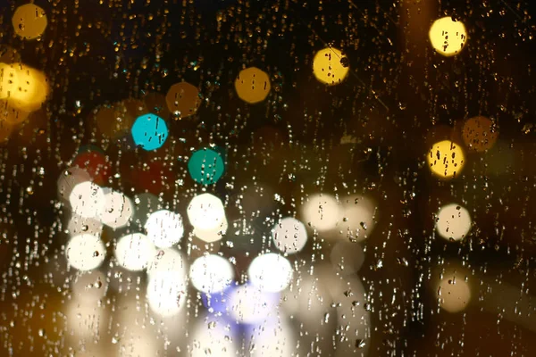 Uzakta parlak renkli bokeh lekeleri olan ıslak cam.