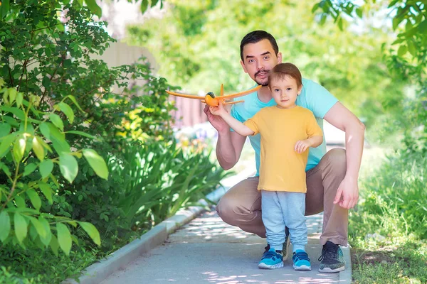 Vater und Sohn beim gemeinsamen Spielen im Freien an sonnigen Sommertagen: Vater und Kind starten orangefarbenes Spielzeugflugzeug. Neuanfang, Elternberatung und Hilfekonzept. — Stockfoto