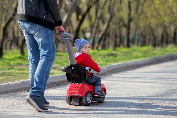 Baba bir bahar yolu boyunca sürme Toddler oğul ile kırmızı Push araba iter. Arka planda ağaçlar. Baba ve oğul birlikte açık yürüyüş. Metin kopyalamak için oda — Stok fotoğraf
