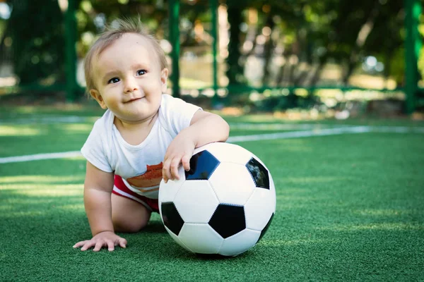 Petit garçon rêveur au stade avec un ballon de foot. Enfant tout-petit souriant sur un terrain de sport avec une balle. Future star du football — Photo