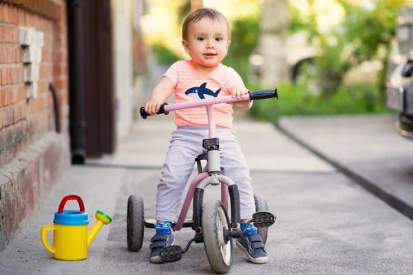 暖かい晴れた日に駐機場の舗装に乗って三輪バイク 三輪車 に乗っている小さな子供の肖像画 小さな水やりは彼の足の近くにすることができます フリータイムキッズアクティビティコンセプト — ストック写真