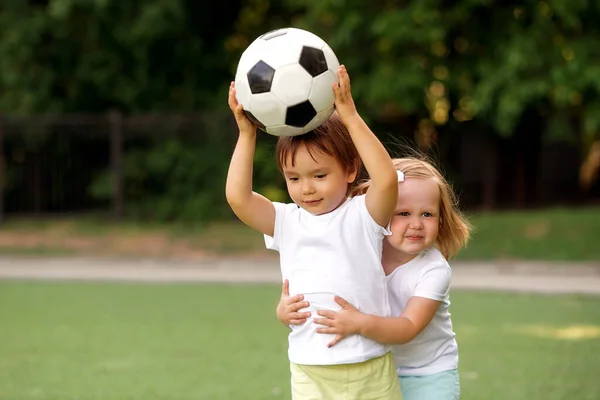 幼稚園でのジムレッスン サッカー場でサッカーボールと一緒に遊んでいる2人の幼児の子供 男の子と女の子 女の子は彼がボールを投げるのを防ぐために 後ろから男の子を保持しています スペースのコピー — ストック写真