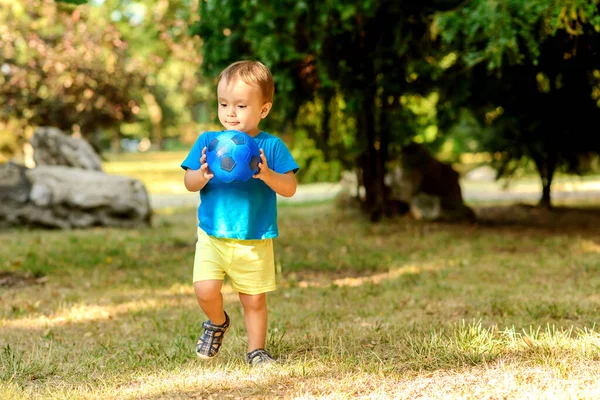 幼児の男の子は晴れた夏の日に芝生の芝生の上で青いサッカーボールで一人で遊んでいる サッカーボールを持っていて 何かを考えている視覚的な小さな子供 子供の頃の夢とスポーツコンセプト — ストック写真