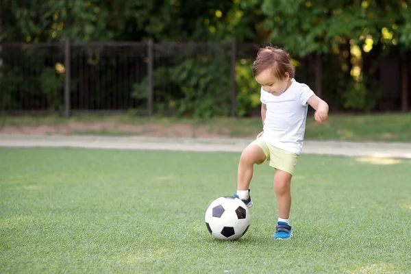 サッカー場でサッカーボールを停止幼児少年 足を上げた小さなサッカー選手は 試合でボールをキックする準備ができています 若い選手と積極的な子供時代のコンセプト スペースのコピー ストック写真
