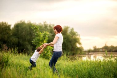 Anne ve küçük oğlu nehir veya göl kıyısında birlikte oynuyorlar. Küçük anne ve küçük çocuk, yaz pikniğinin tadını çıkarıyorlar, birlikte dans ediyorlar. Metni kopyalamak için yer