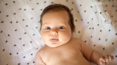 Küçük bebek battaniyeye uzanıp dil gösteriyor. Komik suratlı ve düzgün saç stili olan bir kızın portresi. Yukarıdan bak. Mutlu çocukluk kavramı. Boşluğu kopyala