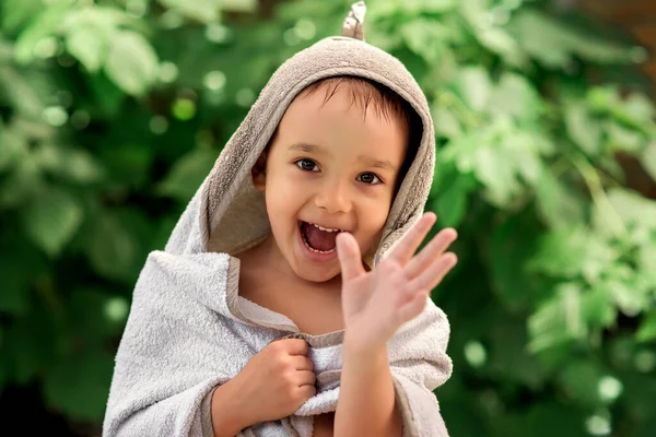 笑顔の幼児の少年は屋外プールで泳いだ後 大きなバスタオルに包まれた 喜んで子供の手を振って笑う 緑の葉を背景に 子供のための夏の活動のコンセプト — ストック写真