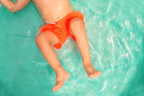 明るいオレンジ色のショートパンツの小さな幼児は スイミングプールで水を遊びます 上からの眺め のんきな子供時代 幸福と自由の概念 — ストック写真