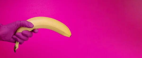 Women Hand with color rubber gloves holding  banana on color background