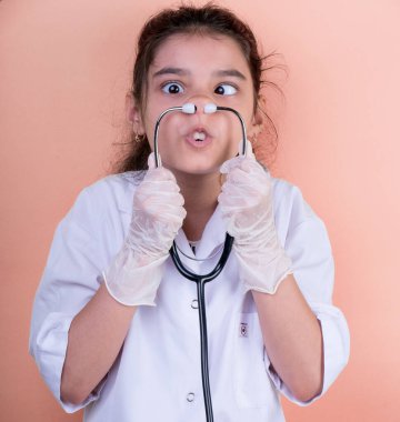 Doktor üniforması giyerken renkli steteskoplu komik bir kız. Heyecan ve cazibe konsepti. Coronavirus geçmişi. Aptal suratlar komik çılgın jestler. Komik ifade. 