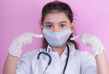 Doktor üniforması giyerken renkli steteskoplu komik bir kız. Renkli maske, panorama. çoklu uzay. Küçük bir doktor portresi. Kovid19. çözülebilir eldivenler 