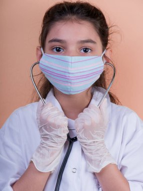 Doktor üniforması giyerken renkli steteskoplu komik bir kız. Renkli maske, panorama. çoklu uzay. Küçük bir doktor portresi. Kovid19. çözülebilir eldivenler 
