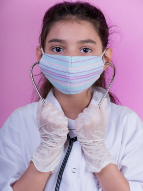 Doktor üniforması giyerken renkli steteskoplu komik bir kız. Renkli maske, panorama. çoklu uzay. Küçük bir doktor portresi. Kovid19. çözülebilir eldivenler 