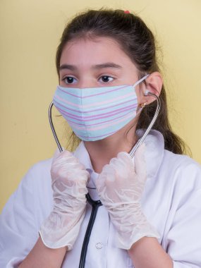 Doktor üniforması giyerken renkli steteskoplu komik bir kız. Renkli maske, panorama. çoklu uzay. Küçük bir doktor portresi. Kovid19. çözülebilir eldivenler 