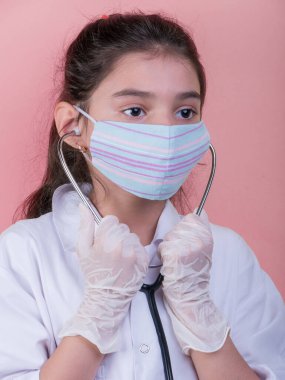 Doktor üniforması giyerken renkli steteskoplu komik bir kız. Renkli maske, panorama. çoklu uzay. Küçük bir doktor portresi. Kovid19. çözülebilir eldivenler 