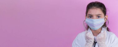 Doktor üniforması giyerken renkli steteskoplu komik bir kız. Renkli maske, panorama. çoklu uzay. Küçük bir doktor portresi. Kovid19. çözülebilir eldivenler 