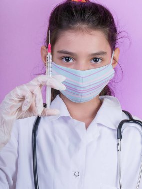 Doktor üniforması giyerken steteskopu ve şırıngası olan komik bir kız. Renkli maskeli Asyalı kız