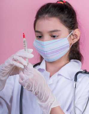 Doktor üniforması giyerken steteskopu ve şırıngası olan komik bir kız. Renkli maskeli Asyalı kız