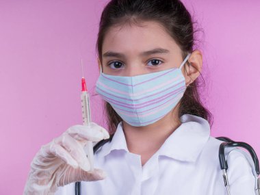 Doktor üniforması giyerken steteskopu ve şırıngası olan komik bir kız. Renkli maskeli Asyalı kız