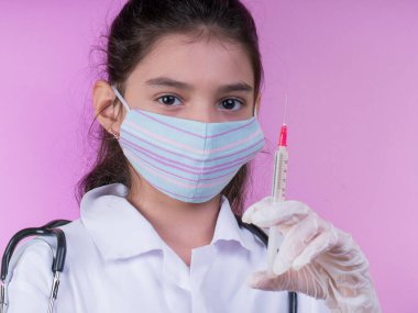 Doktor üniforması giyerken steteskopu ve şırıngası olan komik bir kız. Renkli maskeli Asyalı kız