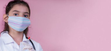 Doktor üniforması giyerken renkli steteskoplu komik bir kız. Renkli maske. Şırınga, covid 19. Aşı