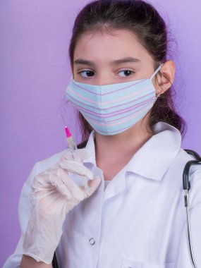 Doktor üniforması giyerken steteskopu ve şırıngası olan komik bir kız. Renkli maskeli Asyalı kız
