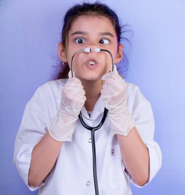 Doktor üniforması giyerken renkli steteskoplu komik bir kız. Heyecan ve cazibe konsepti. Coronavirus geçmişi. Aptal suratlar komik çılgın jestler. Komik ifade. 