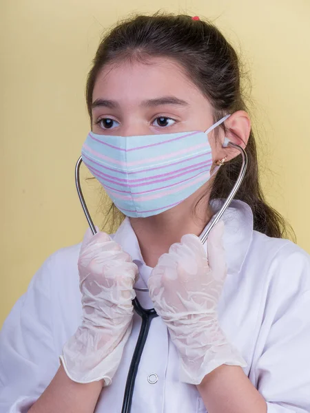 Little funny girl with a collorful stethoscope while wearing Doctor\'s uniform.  colorful mask, panorama . copyspace. portrait a little doctor. covid19. disponsible gloves