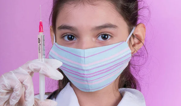 Little funny girl with a stethoscope and syringe while wearing Doctor\'s uniform.  asia girl in colorful mask